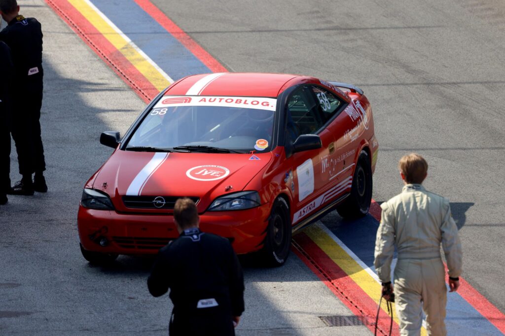 The red Prox car with sponsor decals driving along the pit lane, seen from above