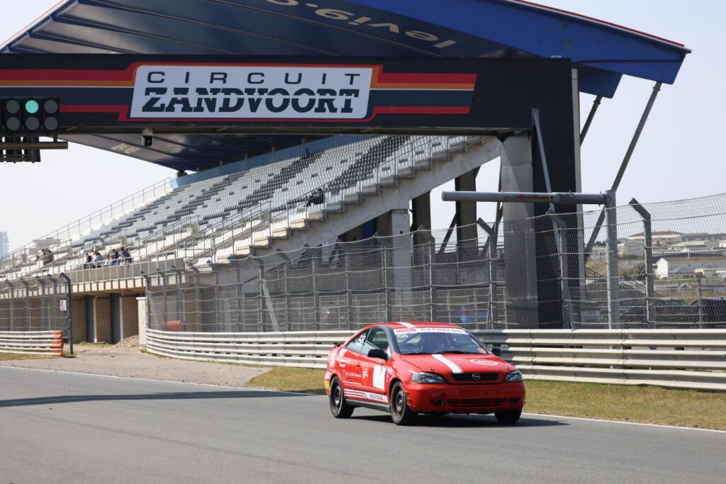 The red Prox car on track below the main grandstand at Circuit Zandvoort