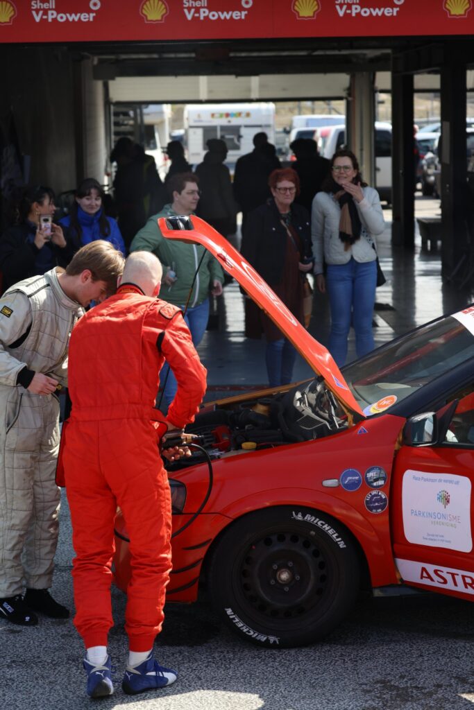 Two team members leaning over the open bonnet of the Prox car in the pit garage while visitors look on
