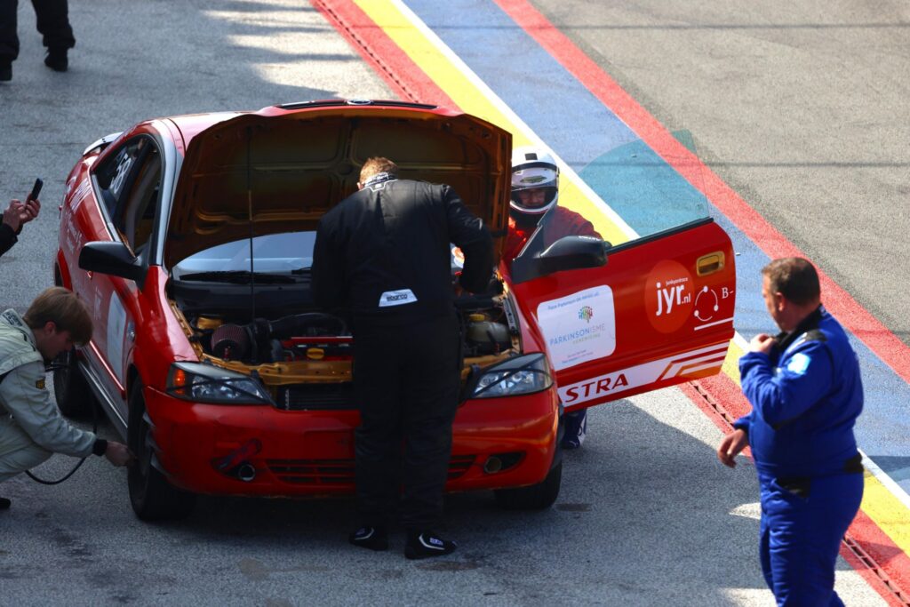 Team members working on the Prox car in the pit lane with the bonnet and door open